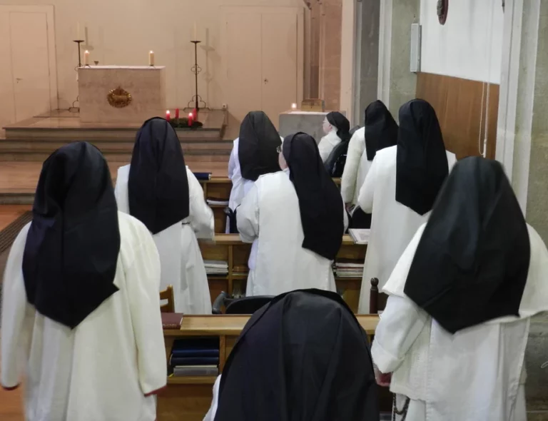 Groupe de sœurs en habit blanc et voile noir priant devant l'autel d'une chapelle avec des bougies et une couronne de l'Avent.